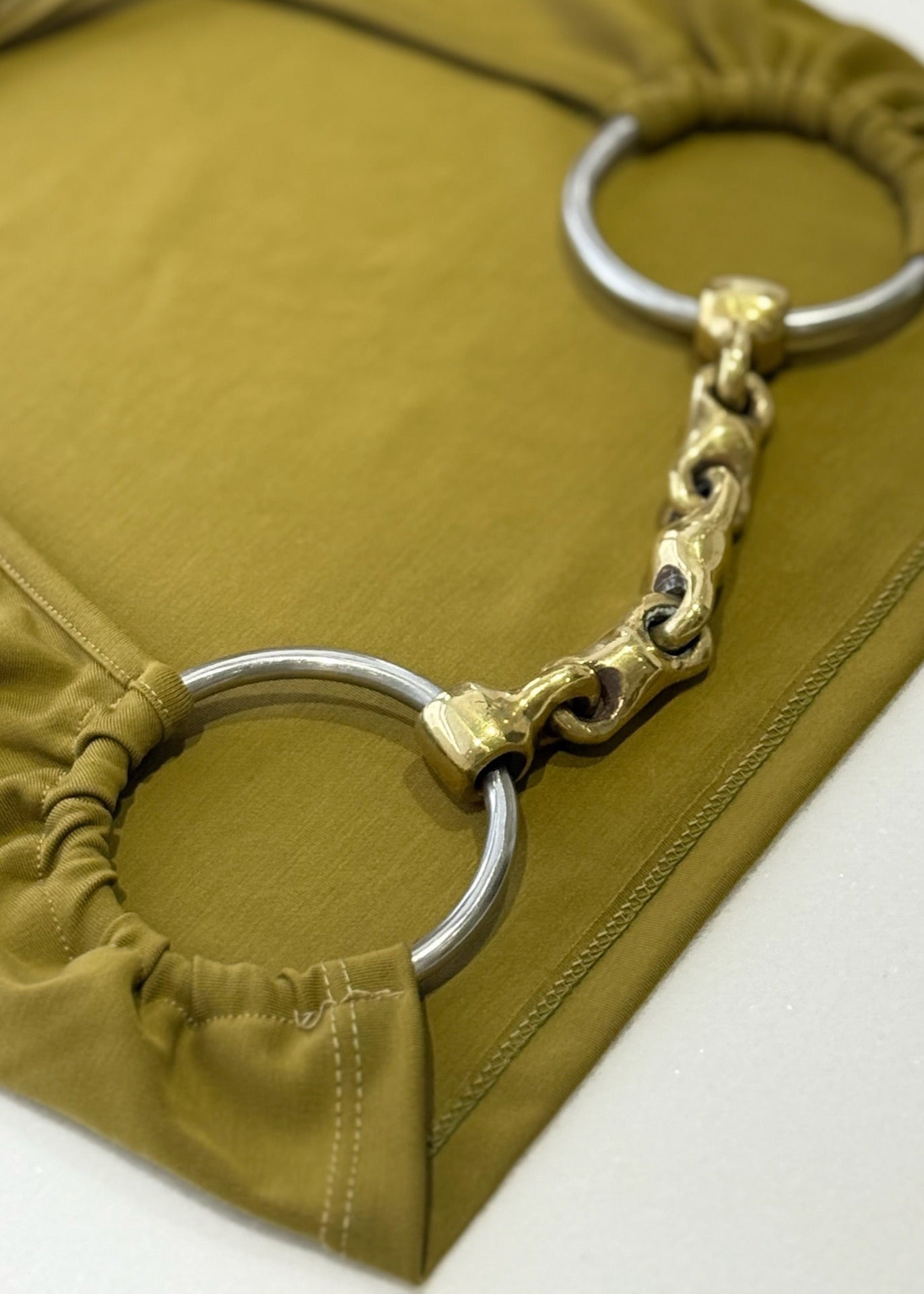 Gold and silver decorative ring on a mustard yellow fabric background horse bit